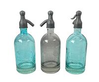 Three seltzer soda bottles, two aqua blue and one clear glass, all with metal siphon tops showing embossed details.