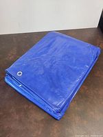 Folded blue polyethylene tarp with visible metal grommets on edges, showcasing thickness and quality of material.