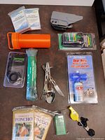 Full layout of the survival and camping equipment including Mylar blankets, ponchos, wipes, utensil, scope mount, lighter, whistle, orange container, and bear horn repellant pack