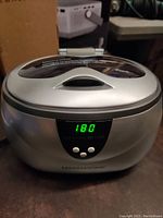 Front view of the Magnasonic ultrasonic cleaner showing digital timer set to 180 seconds with three control buttons and silver top with transparent lid.