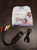 Photo of UCEC branded video capture device with attached RCA cable and packaging showing family image and slogan.