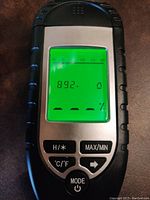 Close up photo of the moisture tester showing a reading of 89.2% moisture content with backlit green screen and control buttons visible.