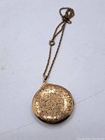 Full view of antique round engraved locket hung on a twisted chain