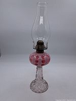 Full view of antique oil lamp showing clear glass chimney, hobnail pink glass reservoir, twisted swirl patterned pedestal and foot