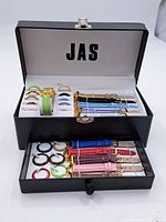 Open black storage case containing a collection of interchangeable watch bezels and leather wristbands, organized in two compartments.