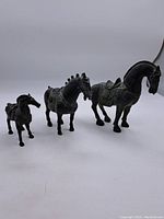 Three metal horse figurines arranged from smallest to largest on a white background showing age-related wear and detailed saddle designs.