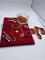 Overview photo showing all items in the lot displayed on red cloth. The photo includes tortoiseshell combs, amber glass bowl, multiple jewelry pieces such as necklaces, rings, hair clips and decorative pins.