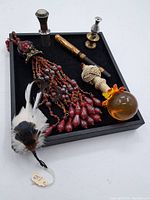 Wide view of all items displayed on a black felt tray showing the large tassel, feather accessory, candlesticks, amber sphere, and gold/black handled item.