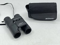 Front view of Nikon Sportstar 8x20 binoculars beside Nikon branded soft carrying case on white surface.