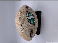 Side view showing CFL and Saskatchewan Roughriders logos with signatures across surface