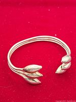 Full view of the sterling silver cuff bracelet with three parallel bands and leaf-shaped ends on a red background.