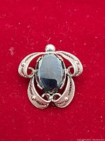 Front view of the vintage sterling silver brooch showing ornamental filigree design with central oval black stone on a red fabric background.