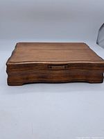 Front view of closed wooden flatware box with curved edges.
