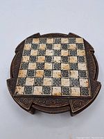 Round travel chess board, closed, showing ornate black and cream carved squares.