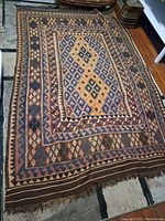 Full view of the vintage Kilim rug spread out, showing the geometric diamond and zigzag pattern in multiple earth-tone colors.
