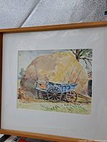 Photo of framed watercolour painting depicting a blue haywagon in front of a large haystack.