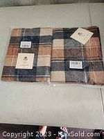 Photo showing two new large scarves folded side by side with tags attached, depicting a soft plaid pattern in neutral colors.
