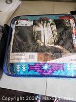 Photo of packaged queen reversible blanket showing outdoor scenic print on packaging and part of blanket pattern