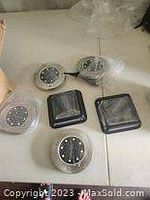 Five solar lights including three round LED solar lights and two square solar panel lights laid out on a flat surface.