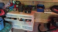Workshop area showing plastic storage drawers with tools and fasteners inside and bins on top, coiled cords to side.