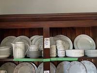 Shelf with plates, bowls, cups, saucers, coffee pot and sugar bowl arranged in wooden cabinet.