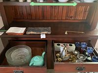 Wide photo showing the items in the drawers and on the shelf: assorted candle holders, candles, a brass candle snuffer, glass bowls, and a ceramic teapot.