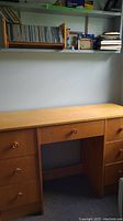 Desk with wall shelves holding a wooden CD holder with CDs and various small picture frames.