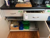 Photo showing plastic food storage containers with various lids stored in a cabinet with drawer above
