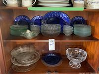 Shelf displaying blue and clear glass dishes including plates and bowls, a large clear glass footed bowl and blue scalloped edge plates arranged in back
