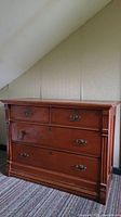 Front view of antique wooden dresser showing four drawers with knocker style pulls, one broken pull visible, carved side details, and keyholes.
