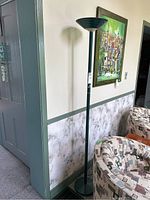 Full view of tall green floor lamp by wall, showing lamp height and placement next to seating furniture.