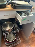 Kitchen unit with open drawer and cupboard showing large Lagostina pot with lid on lower shelf, plus baking pans on bottom shelf.