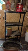 Photo of vintage lanterns, Coleman heater, and copper boiler on shelving unit in shed with other camping gear.