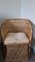 Front angled view of rattan armchair showing woven rattan, black trim, and beige removable seat cushion with button tufting.