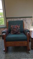 Front view of the rocking chair showing green upholstered cushions and floral throw pillow, solid wood frame with attached armrests