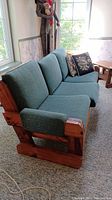 Front angled view of three-seat sofa with green corduroy cushions and two patterned throw pillows resting on the seats.