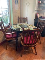 Round dark wood kitchen table with four matching wood arm chairs, each with a red cushion seat, placed by a window in kitchen area.