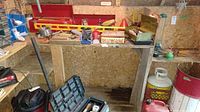 Shelf with multiple red toolboxes, hand tools, and assorted items spread across a wooden shelf and floor beneath.