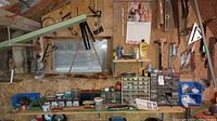 Wide view showing shed wall with parts bins, tools, metal drawers, and items on shelves under a window.