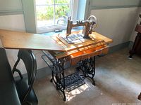 Full image of New Williams treadle sewing machine on wooden table with iron treadle base and foot pedal