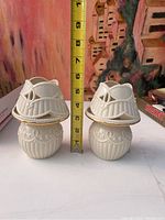 Pair of porcelain tea lamps with intricate design and decorative covers, with ruler for size reference.