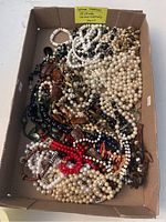 Box containing many different necklaces in various colors and materials including faux pearls, beads, and wood.