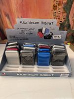 Full display of 16 aluminum wallets arranged in rows, featuring multiple colors and showing product packaging indicating RFID protection.