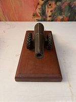 Front view of the iron model cannon statue on a wooden base, showing barrel opening and base detail.
