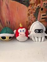 Three Mario Kart plush toys displayed side by side against a painted backdrop, showing details of the faces and colors.