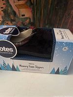 Side view of one pair of Totes Toasties memory foam slippers in box, showing dark corduroy exterior and label with size XL 11-12