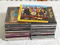 Stack of 23 music CDs including The Beatles Sgt. Pepper's Lonely Hearts Club Band Anniversary Edition and Opus De Jazz Milt Jackson, showing album cover art and titles.