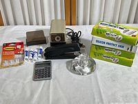 Photo showing all items together including stapler, glue sticks, calculator, paperweight, pencil sharpener, and boxed Wii controller skins.