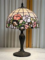 Full view of stained glass table lamp on white surface with floral dome shade and decorative base