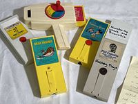 Fisher Price Movie Viewer and six movie cartridges arranged on white cloth background. Close-up of labels showing titles and characters.